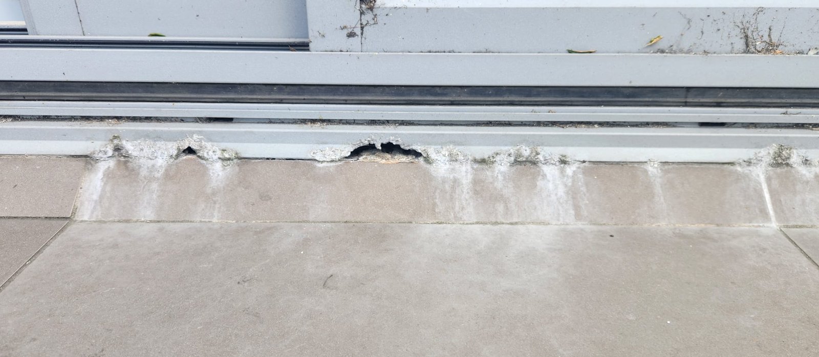 Sliding door sill with pitting along its length and white streaks on the tiles below