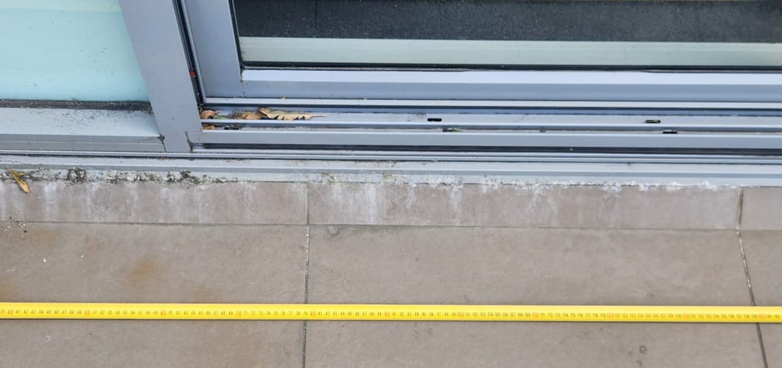 Sliding door sill on another balcony with white deposits along the sill line and tape measure for scale